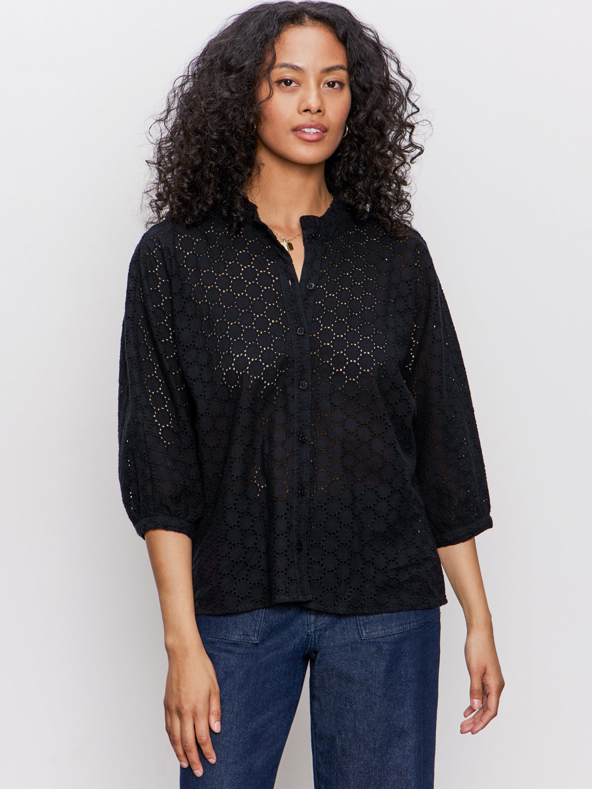 A woman with curly hair wears the Sanctuary Clothing petal drop blouse in black, featuring long sleeves and a scalloped collar, paired with blue jeans against a plain light background.