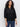 A woman with curly hair wears the Sanctuary Clothing petal drop blouse in black, featuring long sleeves and a scalloped collar, paired with blue jeans against a plain light background.