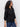 A woman with long curly hair wears the Sanctuary Clothing petal drop blouse in black and blue jeans while standing sideways against a plain light background.