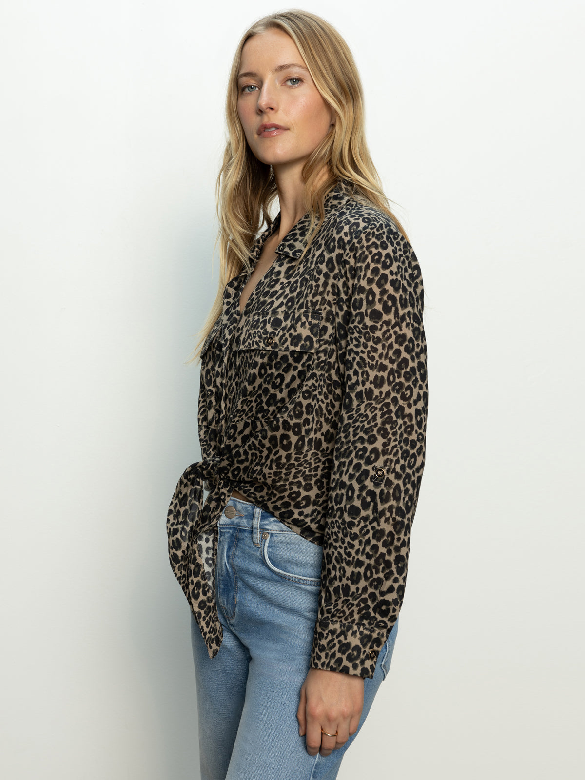 A woman with long blonde hair wears the Sanctuary Clothing "wild love tie top french kitty," a leopard print button-up tied at the waist, paired with light blue jeans against a white background.