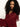 A woman with long, curly dark hair looks down with a calm expression, wearing a sheer, burgundy blouse with ruffled sleeves against a plain, light background.