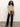 A woman with curly hair models the Sanctuary Clothing "fade into you ruffle blouse" in fawn, paired with high-waisted dark blue wide-leg jeans and black shoes, standing against a plain light background.