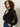 A woman with curly hair models the Sanctuary Clothing serendipity lace tuxedo shirt in black, paired with dark jeans and a studded belt. She poses against a neutral background, gazing thoughtfully to the side.