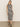 A person with long light hair stands against a plain background wearing the Sanctuary Clothing contrast trim maxi dress in black macrame stripe and black sandals.