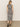 A person with long hair, back to the camera, wears the Sanctuary Clothing contrast trim maxi dress in black macrame stripe and black sandals, standing on a concrete floor against a plain light-colored wall.