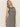 A person with long blonde hair in Sanctuary Clothing's contrast trim maxi dress featuring black macrame stripe is standing against a plain light background. The sleeveless dress has horizontal stripes, and the individual poses with a relaxed expression.