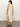 A person with long dark hair stands facing away, wearing the Sanctuary Clothing contrast trim maxi dress in sandstone white stripe. The sleeveless dress is knee-length with a side slit. They sport brown sandals and stand on a plain surface against a neutral backdrop.
