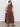A woman with long dark hair and a neutral expression stands on a plain floor against a light gray background, wearing the Sanctuary Clothing "take me away midi dress mesa" in extended sizing and black sandals.