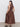 A woman faces away, wearing Sanctuary Clothing's take me away midi dress mesa (extended sizing), a sleeveless brown dress with a fitted bodice and flared skirt, paired with black sandals. She stands on a light floor against a white background.