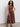 A woman with curly hair wears Sanctuary Clothing’s take me away midi dress in mesa, paired with brown sandals, standing against a plain light-colored background.