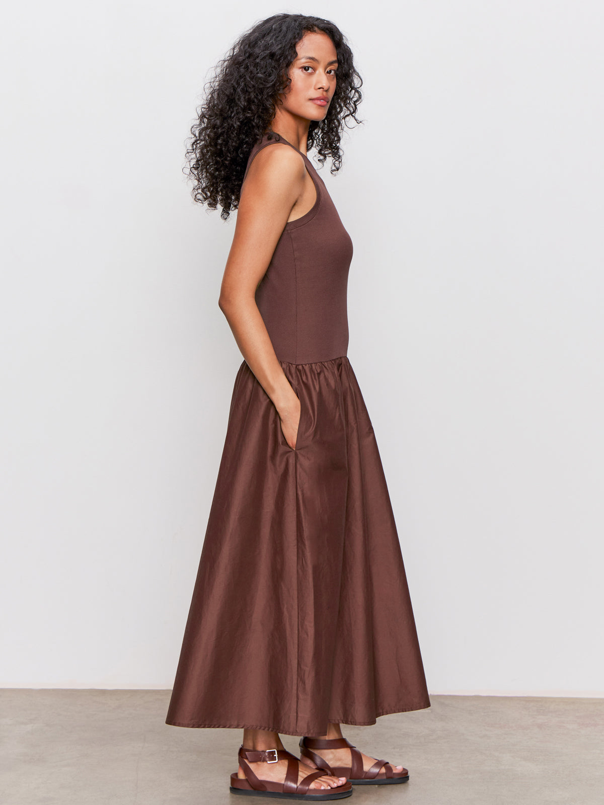 A woman with curly hair stands in profile, wearing the Sanctuary Clothing "take me away midi dress mesa" against a plain white background.
