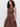 A woman with curly hair models the Sanctuary Clothing "take me away midi dress mesa"—a sleeveless, brown, fitted-top dress with a gathered skirt and pockets—standing against a plain background.