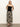 A person stands against a plain white background wearing the meet me at sea midi dress black mirage by Sanctuary Clothing. They have long hair, wear black strappy sandals, and have their hands clasped behind their back.