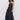 A woman with curly hair models the Sanctuary Clothing "lucky you dress black," a sleeveless, ankle-length dress, paired with black platform sandals, standing against a plain white wall.