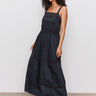 A woman with curly hair models the Sanctuary Clothing "lucky you dress black," a sleeveless, ankle-length dress, paired with black platform sandals, standing against a plain white wall.