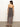 A woman stands indoors facing away, wearing the Sanctuary Clothing effortless slip dress meow—an ankle-length, sleeveless leopard print dress with thin straps and brown sandals. The floor is concrete, background a plain white wall.