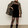 A woman wears the Sanctuary Clothing party shift dress in black, styled with sunglasses, sheer tights, knee-high boots, and a leopard print coat draped over her shoulders, standing against a plain background.