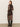 A woman with straight, light brown hair faces away, wearing the "night out mock sweater dress semi sweet" by Sanctuary Clothing and black knee-high boots, standing against a plain light-colored wall.