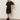 A woman poses against a plain background in the Sanctuary Clothing satin mix tshirt dress black, styled with black knee-high boots and gold hoop earrings. She stands with one hand on her hip and the other relaxed.