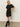 A woman poses against a plain background in the Sanctuary Clothing satin mix tshirt dress black, styled with black knee-high boots and gold hoop earrings. She stands with one hand on her hip and the other relaxed.