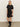A woman with straight blonde hair poses confidently against a light wall, wearing the Sanctuary Clothing satin mix tshirt dress in black and black knee-high boots.