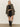 A woman with straight blonde hair and a neutral expression wears the Sanctuary Clothing satin mix t-shirt dress in black, styled simply against a plain wall.