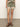 Against a white wall, a person wears Sanctuary Clothing's spring breaker short mezzo sage, featuring brown, pink, and cream patterns. They pair it with brown sandals and a matching top, hands resting at their sides.