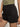The image showcases Sanctuary Clothing's View Cargo Short in black, featuring high-waisted design and buttoned front pockets. The shorts are paired with a tucked-in olive green top, highlighting the waist and upper thighs, with one hand resting by the side.