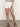 A person wearing Sanctuary Clothing's view cargo short in brilliant white stands against a neutral background. The shorts feature front pockets and button details, paired with a black and white top and brown sandals, with their hands by their sides.