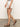 Someone wearing Sanctuary Clothing's view cargo short in brilliant white, with a dark belt and brown strappy sandals, strolls across a smooth, neutral-colored floor. The background is plain and light-colored.