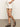 A person in Sanctuary Clothing's arden denim short bleached white pinstripe has hands in pockets, wearing black strappy sandals on a concrete floor against a plain, neutral wall.