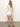 Against a white backdrop, a woman in Sanctuary Clothing™s sleeveless crochet top and arden denim short in brilliant white pairs her outfit with brown sandals. Her hair flows freely as she stands with a relaxed, casual posture.
