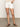 A person in Sanctuary Clothing's arden denim short in brilliant white and a crochet top stands on a concrete floor, sporting brown sandals. The image is cropped at the shoulders to emphasize the outfit.