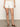 A person is wearing a light patterned top with Sanctuary Clothing's "arden denim short brilliant white." They stand on a gray floor and pair the look with brown sandals, capturing a relaxed summer vibe focused on the lower half of the body.