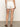 A person stands indoors in arden denim short brilliant white by Sanctuary Clothing, paired with a textured sleeveless top and brown sandals against a neutral-toned background.