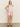 A person in a white tank top, Sanctuary Clothing's "arden denim short washed cherry blossom," and brown sandals stands against a plain beige background, with long hair and posing with one hand on their hip.