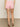 Rear view of someone in Sanctuary Clothing's Arden Denim Short in Washed Cherry Blossom and a white top. The shorts feature back pockets and a rolled hem, while the person stands on a neutral floor, wearing brown sandals.