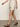 A person is walking, wearing Sanctuary Clothing's caravan cuffed short in flax and a beige top with brown sandals. The image captures their torso and legs against a plain background.