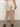 A person in Sanctuary Clothing's caravan cuffed short in flax stands on a concrete floor, back facing the viewer. Their look is completed with brown sandals and a ring on their left hand.