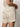 A person is wearing the "caravan cuffed short flax" by Sanctuary Clothing, a beige sleeveless top with matching high-waisted shorts featuring buttoned pockets. Made from light, textured fabric, the outfit stands out against a plain white background.