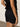 A person wearing the Sanctuary Clothing's voyage short in black and a black sleeveless top with tied bows is standing with their side and back visible against a plain gray background.
