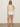 A woman poses against a light background wearing sunglasses, a sleeveless beige crochet top, beige sandals, and Sanctuary Clothing's voyage short in bleached white. She has one hand on her hip and looks relaxed.