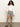 A woman with long curly hair stands against a plain background, wearing Sanctuary Clothing™s voyage short yacht stripe, a white cropped jacket, and black slide sandals, one hand in her pocket and a relaxed expression.