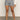 A person wearing the Sanctuary Clothing voyage short yacht stripe shorts, a white long-sleeve top, and black sandals stands on a smooth floor against a plain backdrop. Their face is not visible.