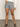 A person wearing the Sanctuary Clothing voyage short yacht stripe shorts, a white long-sleeve top, and black sandals stands on a smooth floor against a plain backdrop. Their face is not visible.