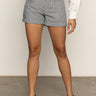 A person wearing the Sanctuary Clothing voyage short yacht stripe shorts, a white long-sleeve top, and black sandals stands on a smooth floor against a plain backdrop. Their face is not visible.