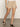 A person is wearing the Sanctuary Clothing liner short in sandstone, paired with a white top and black sandals, standing on a gray floor against a plain light wall. The image focuses on the lower half of the body.