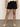 Only the lower half of a person is shown, wearing Sanctuary Clothing’s cruiser short black with a white knit top and cream woven flats, standing against a plain wall.