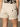 A person is seen from behind wearing the Sanctuary Clothing cruiser short in washed sandstone, featuring rolled hems and back pockets, paired with a black and beige patterned top.
