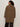 A person with curly hair and glasses is seen from behind, modeling the Sanctuary Clothing hometown jacket lynx extended sizing€�a knee-length, brown and black leopard-print coat€�against a plain light background.